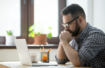 young bearded manager working and reading data on laptop in home office